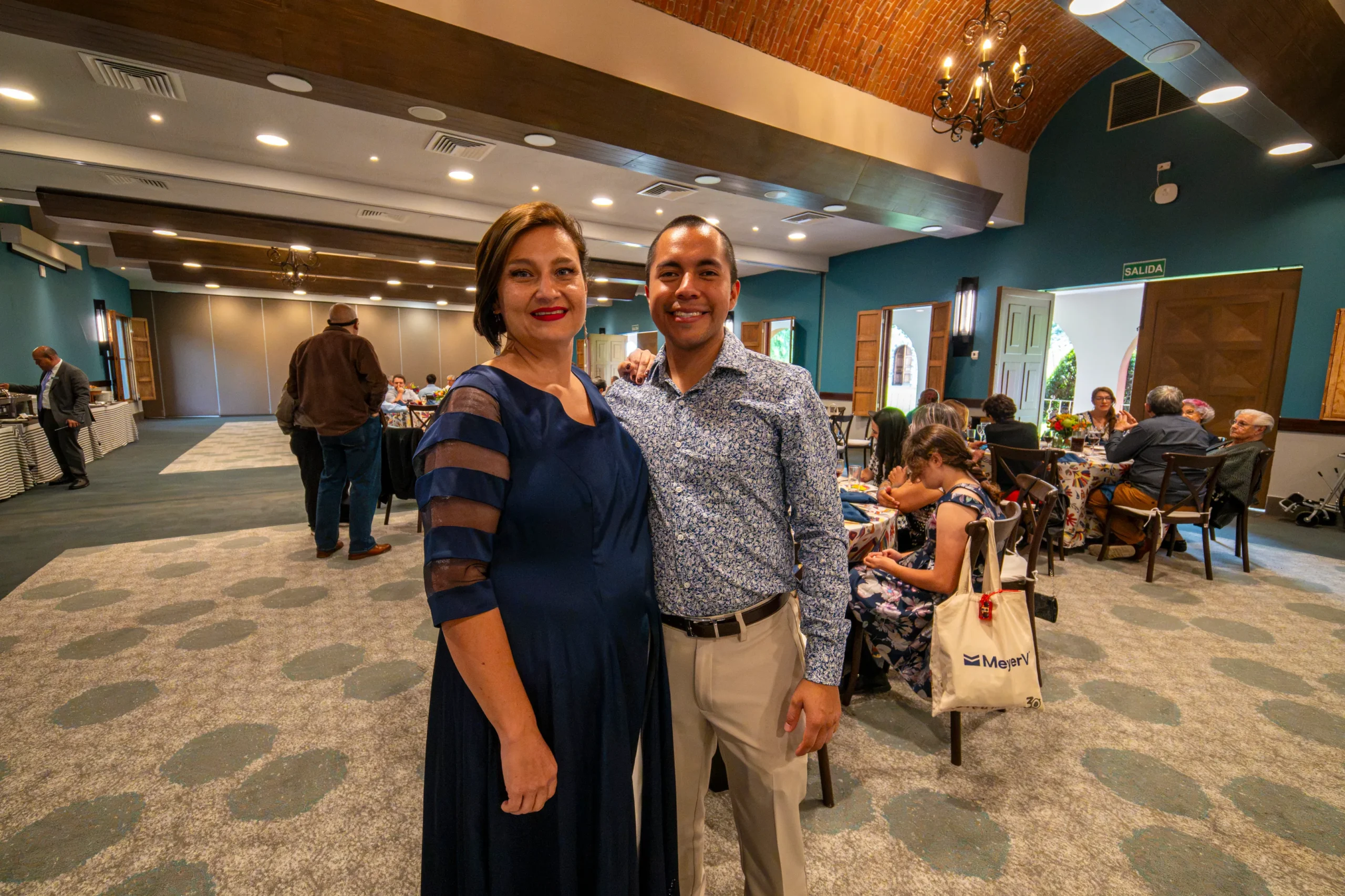 Un hombre y una mujer posando sonrientes juntos en el salón principal durante un evento corporativo.